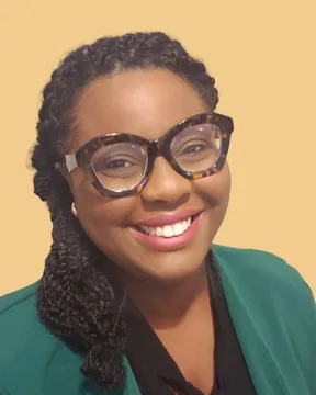 Denise Robinson, smiling, in a green jacket against a warm gold background