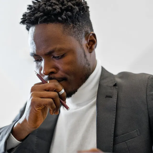 A person reading closely, pen in hand, thinking something over